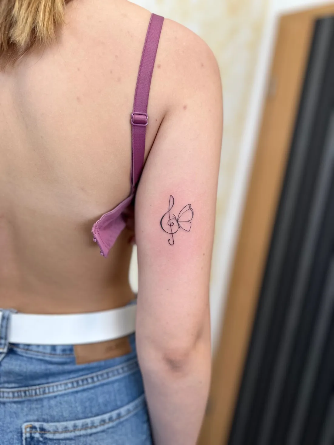Notenschluessel mit Schmetterling am Oberarm — Fine Line Tattoo von Marko